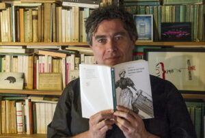 uomo con un libro tra le mani, volto e busto verso la fotocamera che scatta la foto