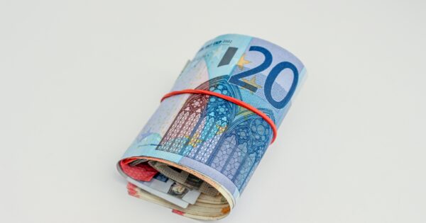 rotolo di soldi con attorno un elastico rosso, banconota più all'esterno di venti euro, sfondo bianco