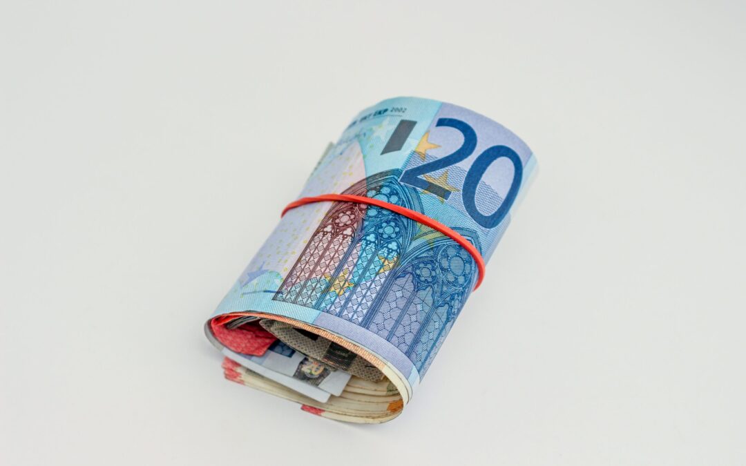 rotolo di soldi con attorno un elastico rosso, banconota più all'esterno di venti euro, sfondo bianco